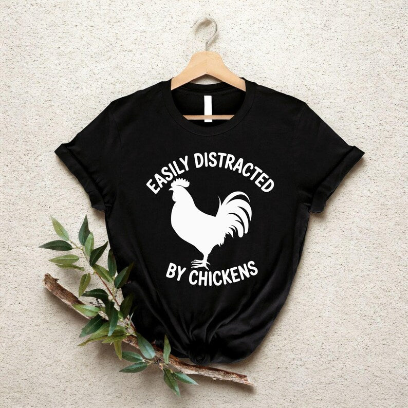 Easily Distracted By Chickens T Shirt created for chicken lovers, backyard chicken keepers, poultry farmers, homesteaders, smallholders, country lifestyle enthusiasts, farm animal lovers, rural families, and anyone who can't resist stopping to admire chickens. Featuring a bold chicken silhouette with modern typography, this premium graphic tee from Teezora Prints celebrates farm life while offering exceptional comfort, premium print quality, stylish everyday fashion, and a fun personality for poultry enthus