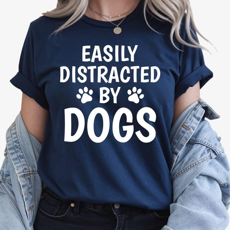 Let everyone know where your attention goes with this Easily Distracted by Dogs graphic t-shirt. The bold slogan and cute paw print design create the perfect combination of humour and style for every dog lover. Soft premium cotton and professional printing ensure lasting comfort, with every shirt proudly printed in the UK by TeezoraPrints.