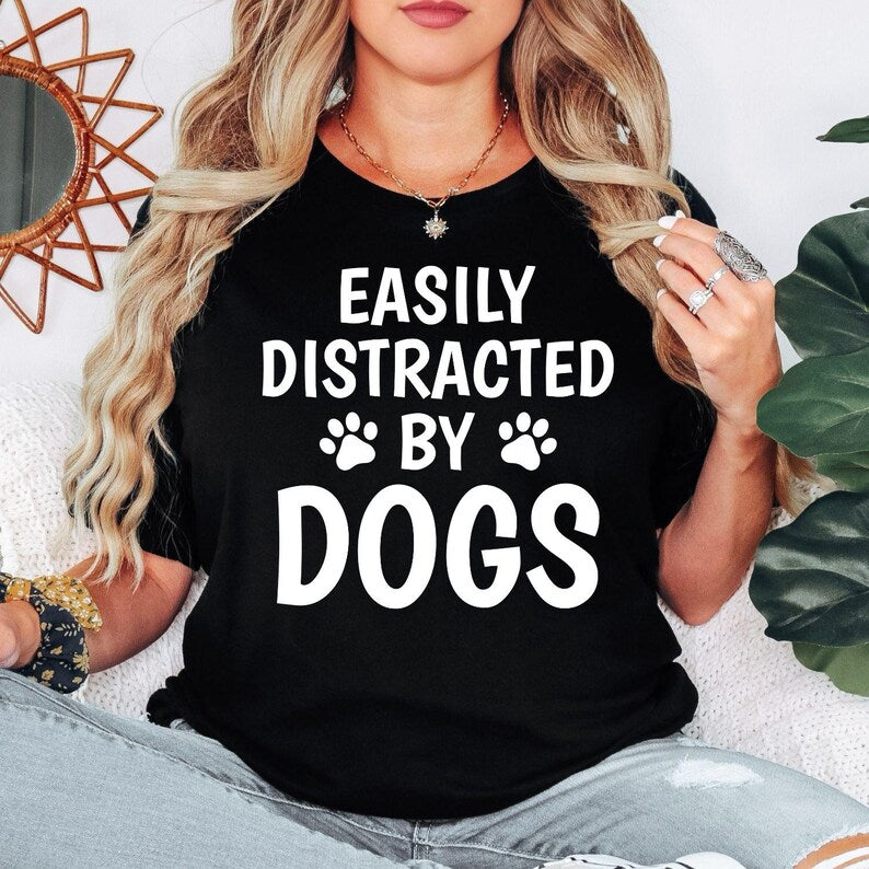 Perfect for dog lovers, pet parents, puppy owners and animal enthusiasts, this Easily Distracted by Dogs shirt features bold typography with adorable paw prints, making it a fun everyday choice. Whether you're walking your dog, visiting the park or relaxing with your favourite companion, this premium graphic tee offers lasting comfort. Professionally printed in the UK by TeezoraPrints using high-quality materials.