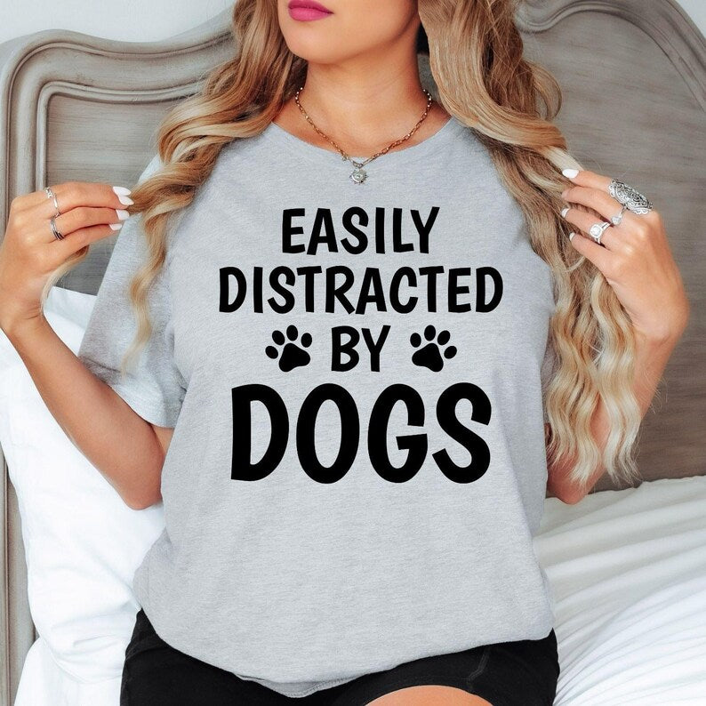 Celebrate your love for dogs with this Easily Distracted by Dogs shirt featuring bold typography and playful paw print graphics. Whether spending time with your pet, travelling, relaxing at home or exploring outdoors, this premium t-shirt offers comfort and style. Every order is proudly printed in the UK by TeezoraPrints for lasting quality.
