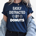 Show everyone your love for sweet treats with this Easily Distracted by Donuts graphic t-shirt featuring bold typography and fun donut icons. The soft premium cotton and relaxed unisex fit make it perfect for everyday wear. Every order is made to order and professionally printed in the UK by TeezoraPrints with exceptional attention to detail.