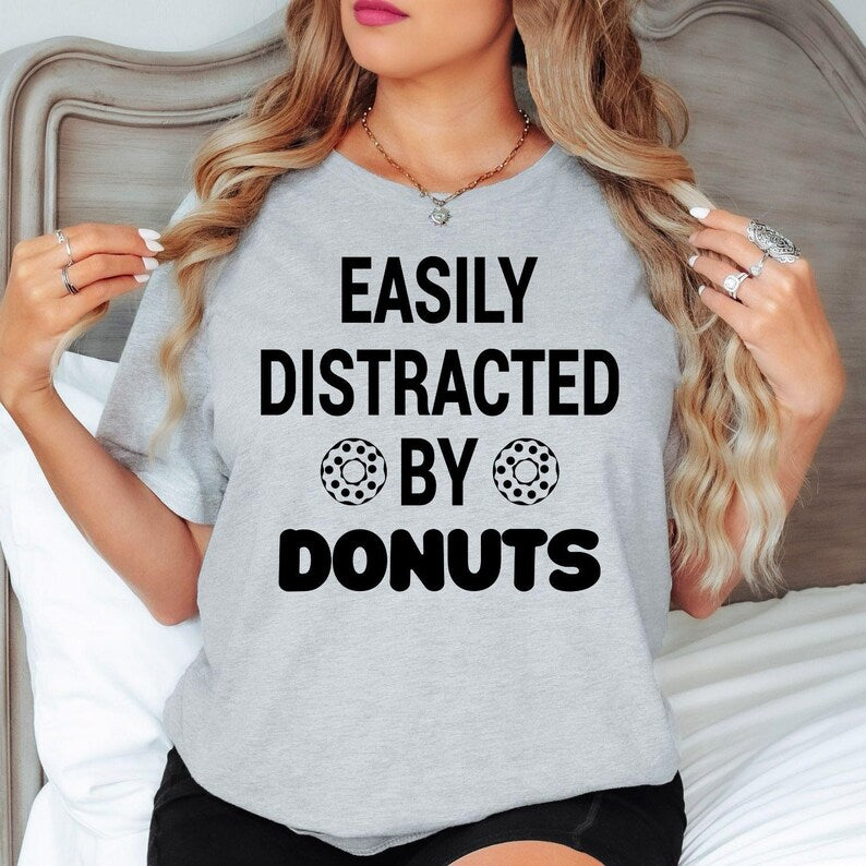 Celebrate your love for donuts with this Easily Distracted by Donuts shirt designed for people who can never resist a sweet treat. Whether you're enjoying coffee, exploring local bakeries or spending time with friends, this premium graphic tee delivers all-day comfort. Every shirt is proudly printed in the UK by TeezoraPrints for exceptional quality.