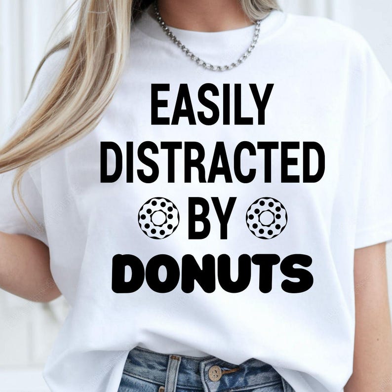 Easily Distracted by Donuts shirt, funny donut lover t shirt, bakery lover tee, foodie shirt, dessert lover apparel, coffee lover clothing, sweet tooth gift, donut graphic tee, novelty food shirt and humorous casual fashion. Every premium t-shirt is proudly printed in the UK by TeezoraPrints for long-lasting comfort and quality.