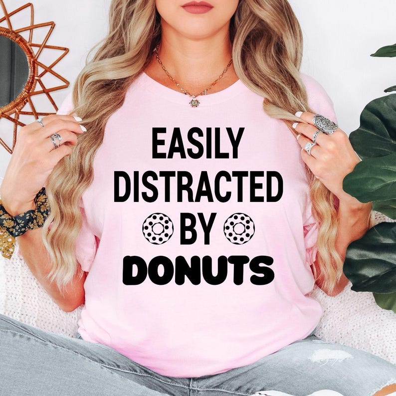 Perfect for donut lovers, bakers, foodies and anyone with a serious sweet tooth, this Easily Distracted by Donuts shirt features bold typography with playful donut graphics for a fun everyday look. Ideal for casual outings, bakery visits and coffee dates. Every premium t-shirt is professionally printed in the UK by TeezoraPrints using high-quality materials for exceptional comfort.