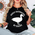 Funny Easily Distracted by Ducks shirt featuring a bold duck silhouette and eye-catching typography for bird lovers and wildlife enthusiasts. Perfect for nature walks, bird watching, park visits and casual everyday wear. Every premium graphic t-shirt is professionally printed in the UK by TeezoraPrints with vibrant print quality and exceptional comfort.