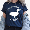Perfect for duck lovers, bird enthusiasts, wildlife fans and nature lovers, this Easily Distracted by Ducks shirt features a bold duck silhouette with playful typography for a fun everyday look. Whether you're visiting the park, relaxing by the lake or enjoying the countryside, this premium t-shirt delivers lasting comfort. Every shirt is professionally printed in the UK by TeezoraPrints using premium-quality materials.
