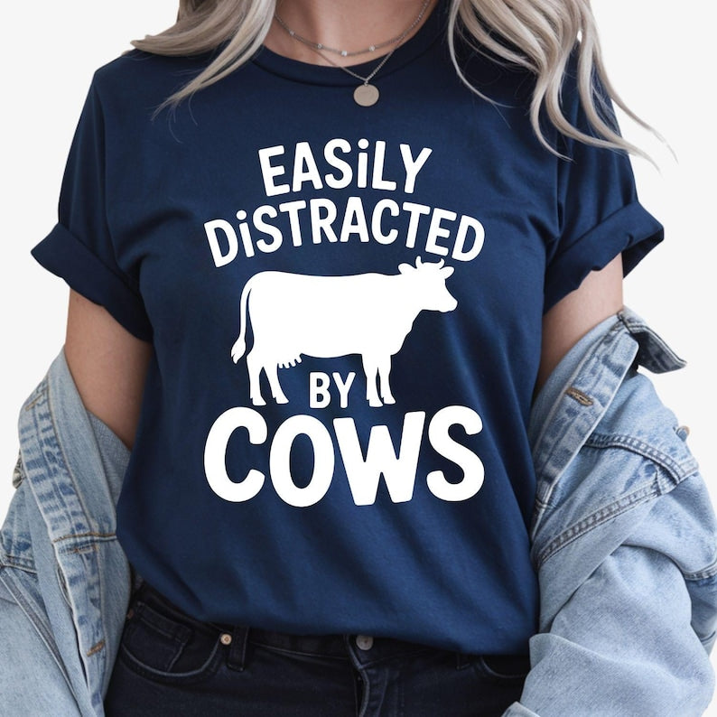 Funny Easily Distracted by Cows shirt designed for cow lovers, farmers, ranchers, dairy workers and anyone who enjoys country life. Featuring a bold cow silhouette and playful slogan, this premium graphic t-shirt is perfect for everyday wear on the farm or in town. Professionally printed in the UK by TeezoraPrints, offering exceptional comfort, quality and long-lasting durability for every animal enthusiast.