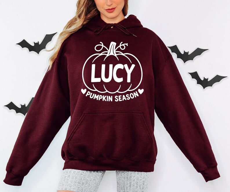 Personalised autumn hoodie with a custom name displayed inside a pumpkin illustration and Pumpkin Season wording. Designed as a cosy seasonal clothing choice for pumpkin picking, Halloween events, autumn celebrations and casual everyday wear. A unique personalised gift idea for pumpkin lovers, family members, friends, mums, sisters or anyone who enjoys the autumn season.